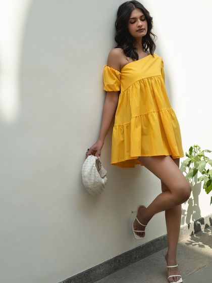 A full-length look for Itgirl Love, showcasing a one-shoulder yellow dress paired with a white woven bag. The clean background and natural light create a fresh and modern e-commerce image.