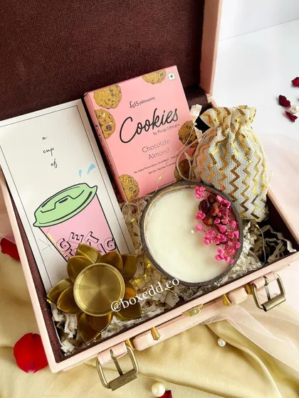 A beautiful pink trunk hamper for Diwali, filled with cookies, a scented candle, a decorative diya, and a potli bag. This is a perfect example of a gift that employees and clients will love and remember.