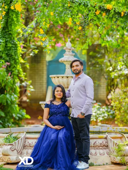 A classic couple's portrait by a garden fountain, with the mother-to-be in a beautiful blue gown.