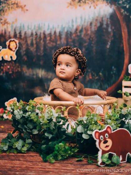 Looking off into the distance, perhaps spotting a friendly lion. The forest backdrop and props create a magical setting for these imaginative baby portraits.
