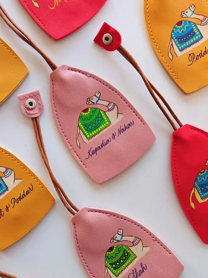 An array of colorful, hand painted leather keychains, each personalized for different families like 'Kapadia & Nahar' and 'Mittal & Poddar'. These make for wonderful, bespoke wedding or event favors.
