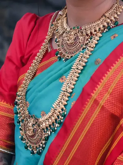 A close-up of the bride's torso, showcasing the magnificent traditional gold necklaces against her vibrant turquoise and red saree.