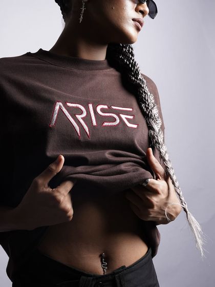 A trendy, cropped shot of the 'ARISE' t-shirt, revealing a belly piercing. This styling choice adds an edgy, personal touch that resonates with a younger demographic.
