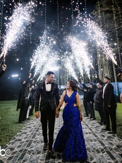 A grand entrance for a lifetime of happiness. The couple walks hand-in-hand under a brilliant arch of cold-pyro fireworks, creating a truly cinematic moment for their Sangeet night.