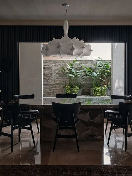 The dining room is a dramatic space with a massive stone table and a sculptural white chandelier. A large window looks out onto a green courtyard, bringing a sense of nature indoors.