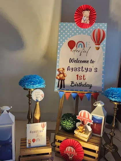The full entrance decor setup. A personalized welcome board on an easel is surrounded by themed props like lanterns, paper fans, and a small gift box, creating an inviting entryway.