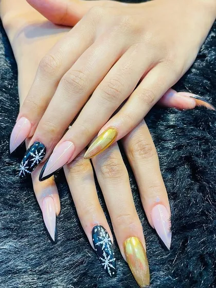 A dramatic winter-themed set with long stiletto nails, black snowflake art, and a gold chrome accent.