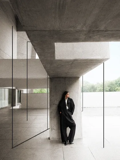 The interplay of light, shadow, and concrete creates a dramatic backdrop. The styling is kept simple and dark to create a strong silhouette against the architectural forms.