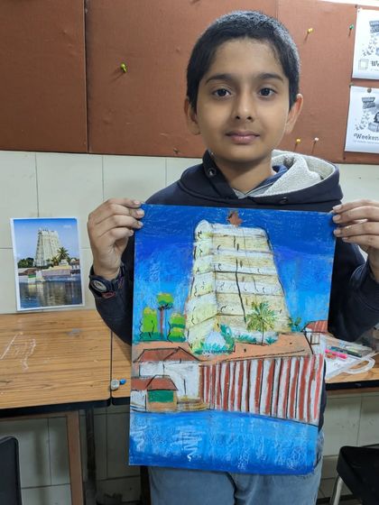 This student proudly presents his detailed oil pastel drawing of a temple, showing his careful attention to the reference photo.