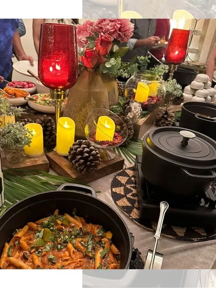 A warm and inviting Diwali buffet table, decorated with red lanterns, candles, and pinecones, featuring a delicious spread of pasta and other dishes.