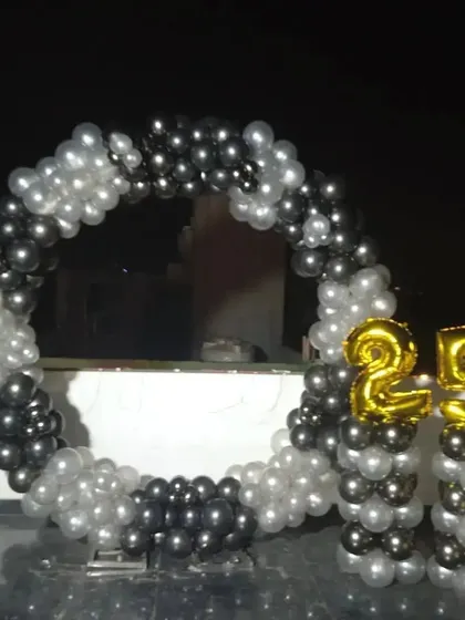A simple and modern outdoor balloon ring for a 25th birthday. The black and silver balloons create a sleek look, complemented by gold foil numbers on pillars.