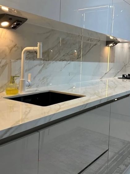 A close-up on the details: a high-arc white faucet over a black granite sink, set against a glossy marble-patterned countertop and backsplash. The handle-less cabinets and under-cabinet task lighting complete the modern look.