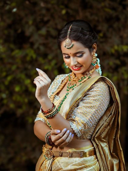 A happy bride showcasing our green-stoned temple jewellery set. The vaddanam, or waist belt, cinches the saree beautifully, completing the traditional silhouette.