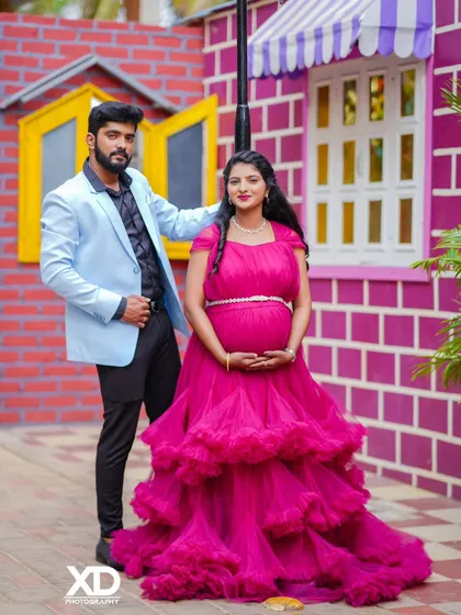 A full-length portrait of a stylish couple against a colorful brick wall.