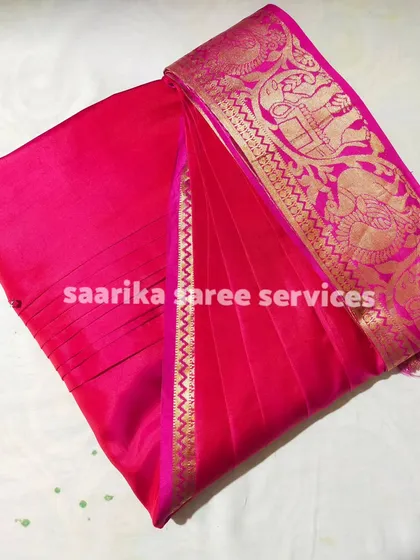 A bright pink saree with a unique gold border, folded and ready for a customer.
