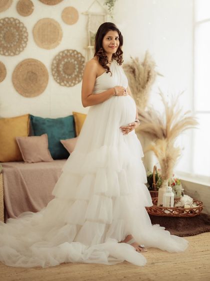 A full-body shot of a mom-to-be in a beautiful white tiered gown, looking serene in our earthy-toned boho studio.