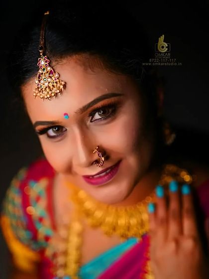 This studio portrait uses dramatic lighting to create a captivating look. The light from above highlights the intricate maang tikka and the model's expressive eyes, while the vibrant colors of her saree pop against the dark background.