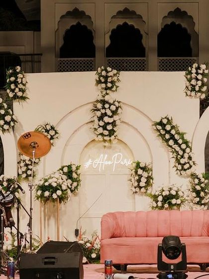 The Sangeet stage, with a soft pink sofa set against a backdrop of white arches and abundant white floral decor, creating a romantic and elegant look.