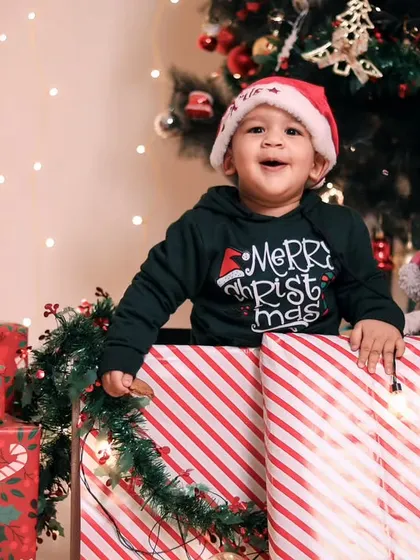 A close-up of the happy baby in the Christmas gift box, surrounded by presents and a teddy bear.