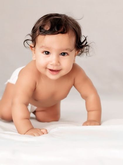 A baby boy crawling on a white sheet.