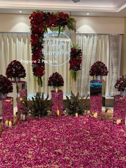 A closer view of our indoor proposal setup, highlighting the custom "Will you marry me?" neon sign inside a floral arch. The arrangement uses bouquets of deep red roses on mirrored pedestals of varying heights to add depth and luxury.