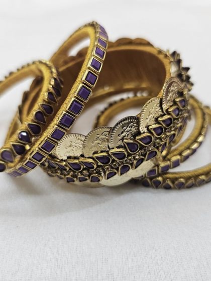 A closer look at the craftsmanship of the purple and gold coin bangle set, showing the detailed arrangement of kundan stones and antique-finish coins on a silk thread base.