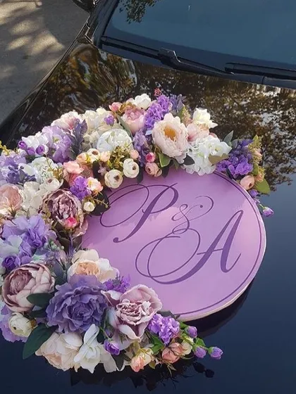 A personalized floral ring for a wedding car. This arrangement features the couple's initials on a lavender plaque, surrounded by a wreath of beautiful artificial flowers in matching shades.