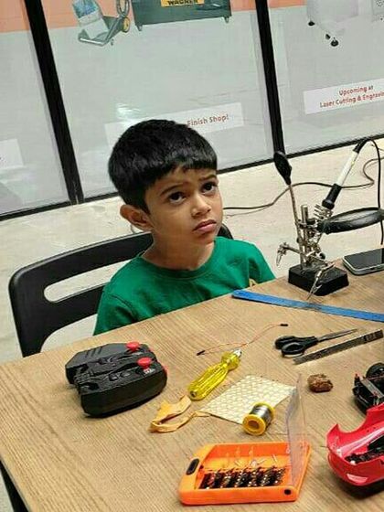 A young boy contemplates a disassembled remote control car at his workbench. These moments of thoughtful problem solving are where true learning happens, as kids figure out how to put the pieces back together.