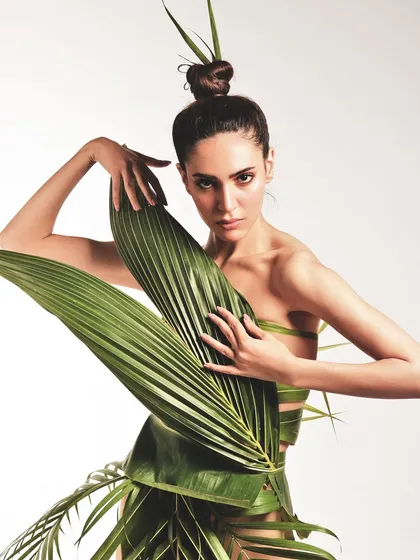 This angle showcases the intricate construction of the leaf dress and the clean, polished beauty look that accompanies it.