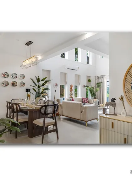 An open-plan living and dining area in Goa, filled with natural light and greenery. The space feels bright and connected, with a clear view from the dining table through to the living room and the lush outdoors.