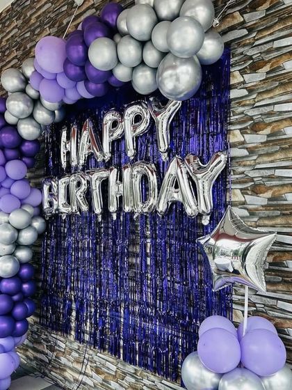 A birthday setup with a purple and silver balloon arch against a purple shimmer curtain.