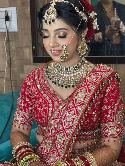 A soft, candid moment of a bride in a red lehenga. The makeup features a subtle glow and shimmery eyeshadow, paired with a classic red rose bun for a touch of romance.