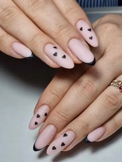 A moody and romantic design with a matte nude base, black French tips, and tiny black hearts.