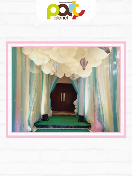 A dreamy entrance with a ceiling of fluffy clouds and hanging hot air balloons, creating the feeling of walking through the sky.
