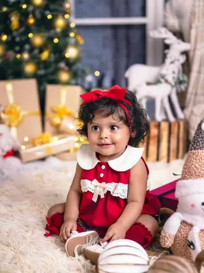 This little girl in a festive red dress is surrounded by presents and holiday cheer, her smile lighting up the room.