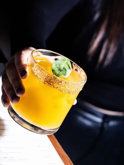 The Ahh!!! Man-go mocktail, captured in a moment of enjoyment. The rim is dusted with a sweet and spicy mix, adding an extra layer of flavor to this tropical refresher.