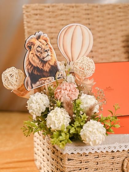 The floral arrangement for this baby hamper was designed to match the safari theme, with a lion and hot-air balloon cutout nestled among soft, neutral-toned flowers.