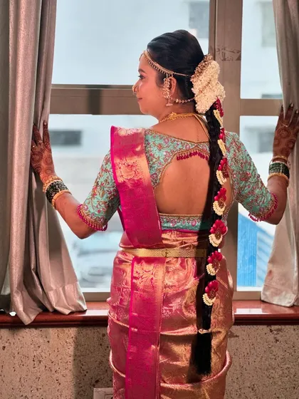 A lovely view of a bride's traditional floral braid from the back. The hairstyle features a long plait decorated with jasmine and red flowers, perfect for her Muhurtham ceremony.