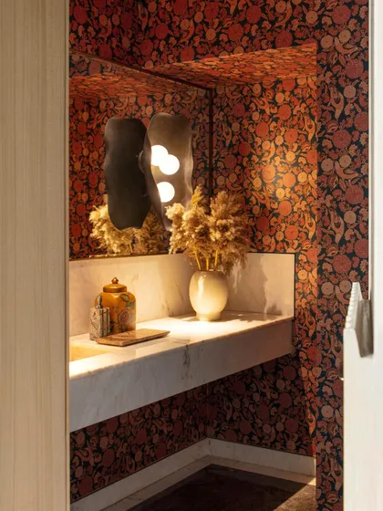 Inside the Bammi Residence powder room, a bold Sabyasachi wallpaper creates a luxurious and evocative backdrop. A sculptural wall sconce and a marble vanity complete the opulent look.