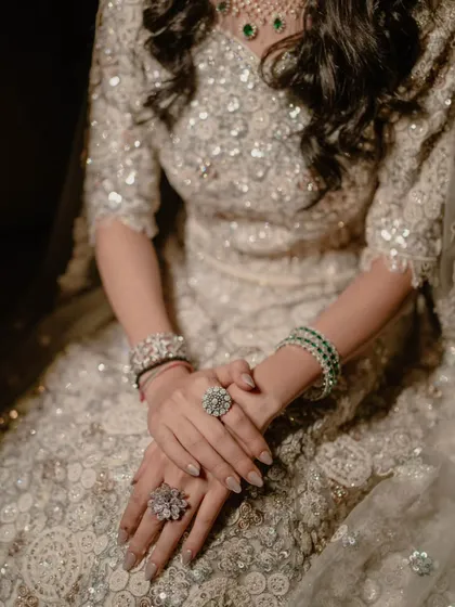 A close-up on the bride's hands, showcasing her sparkling rings and bracelets against her intricately sequined lehenga.