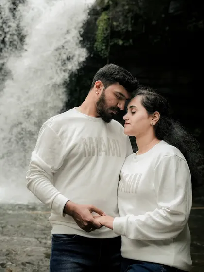 A quiet, intimate moment in front of the waterfall. The couple holds hands, their expressions full of love and tenderness, showcasing a deep and gentle connection.