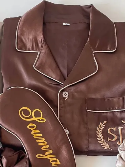 A detailed look at our personalised satin night suit for the bride or bridesmaid. This rich brown set features custom embroidery with initials in a laurel wreath and a matching sleep mask with the name 'Soumya'.