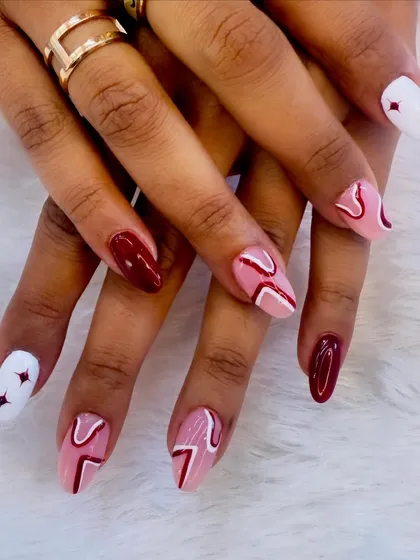 A modern and graphic design in red and white. This set combines solid maroon nails with abstract line work and starburst accents for a bold look.