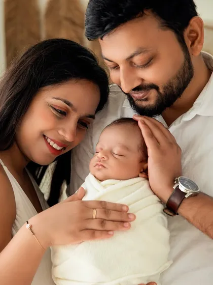 A close-up of the family, showing their gentle hands on their sleeping baby. A portrait of unity and love.