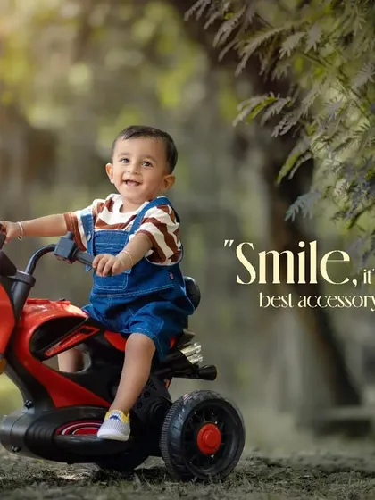 Smile, it's your best accessory. A happy boy on his red toy motorcycle, with his guitar resting against a nearby tree.