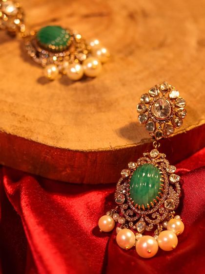 A pair of elegant earrings featuring a large carved emerald surrounded by polki diamonds and finished with pearl drops. A timeless design to make a lasting impression.