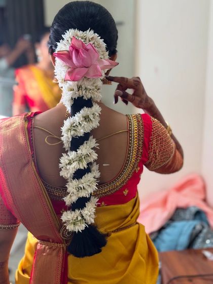 A view of the beautiful traditional floral hairstyle created for Dr. Sushmita's Muhurtham. The braid is adorned with fresh jasmine and a stunning pink lotus, adding a touch of natural elegance.