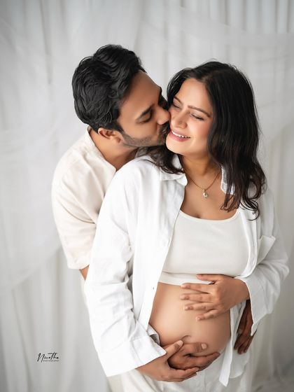A happy and intimate moment between an expecting couple, captured against a clean, white backdrop.