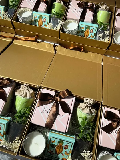 The beauty is in the details. This is a close-up of our sustainable and wellness-themed corporate hampers, featuring live plants, scented candles, and artisanal chocolates. The color coordination of green, pink, and gold creates a soft, premium aesthetic.