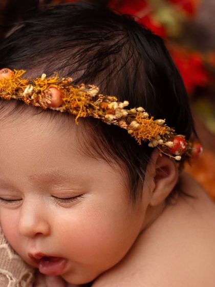 A close up on this sleeping baby's face, showing her soft cheeks and parted lips. The details of the autumn-toned floral crown add a beautiful touch.